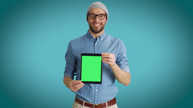 Mittelschuss-eines-schmelzenden-Moalen-Menschen,-der-sich-an-uns-Tablet-Computer-mit-isolierten-Mock-up-Green-Screen-vorstellt.-Schuss-auf-einen-Teal-Colored-Hintergrund.
