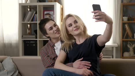 Zwei-junge,-schöne-Mädchen-sitzen-auf-der-Couch-und-machen-Selfies,-Lesben,-LGBT.-60fps