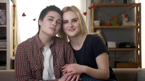 Zwei-junge-lesbische-Mädchen-sitzen-auf-der-Couch,-schaut-in-die-Kamera-halten-Hände,-Knuddeln,-kuscheln,-Liebe,-Care,-Familienidylle-60fps