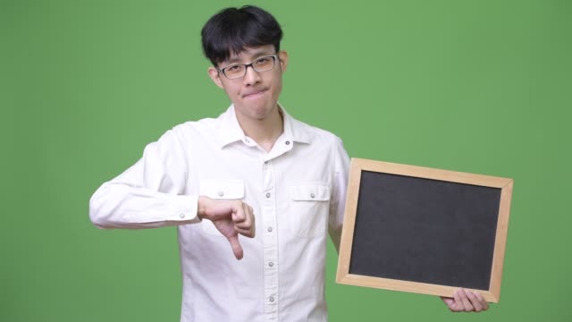 Young-Asian-businessman-holding-blackboard-while-giving-thumbs-down