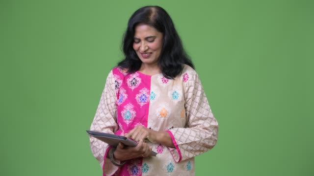 Mature-happy-beautiful-Indian-woman-using-digital-tablet-while-thinking