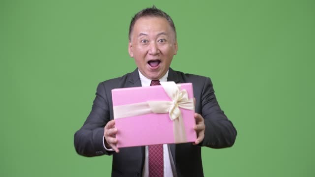 Reife-japanischer-Geschäftsmann-mit-Geschenk-Box-vor-grünem-Hintergrund