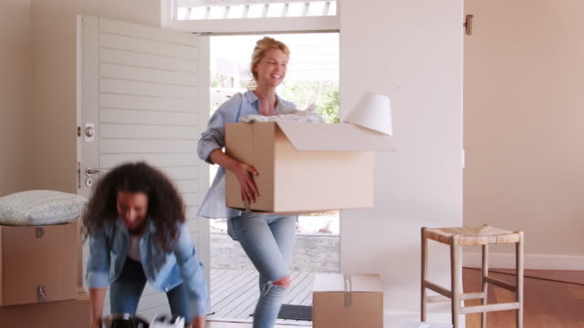 Female-Friends-Carrying-Boxes-Into-New-Home-And-Celebrating-On-Moving-Day