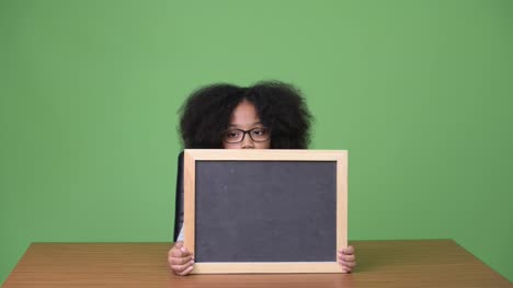 Young-cute-African-girl-with-Afro-hair-showing-blackboard-while-sitting