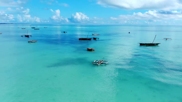 Vista-aérea-de-un-pescador-navega-en-un-barco-de-madera-en-agua-azul-clara-a-lo-largo-de-una-playa-exótica-tropical-en-África