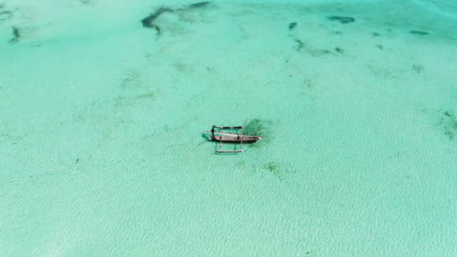 Luftaufnahme-eines-Fischers-Segel-auf-einem-Holzboot-auf-dem-klaren,-blauen-Wasser-entlang-einem-tropischen-exotischen-Strand-in-Afrika