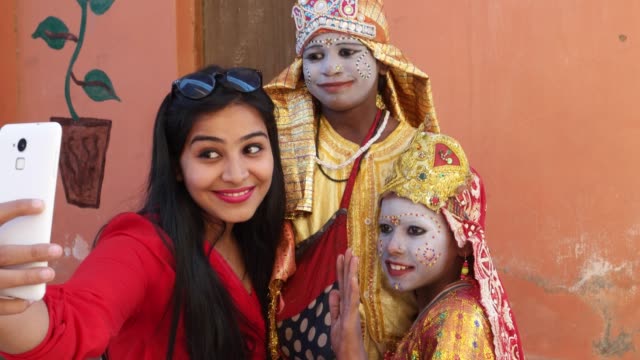 Handheld-shot-of-an-urban-Indian-female-tourists-with-two-females-dressed-as-goddess-taking-selfie-photography-making-video