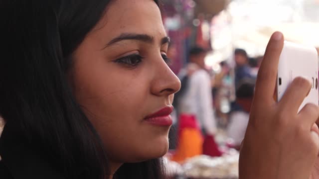 Nahaufnahme-eines-hübschen-Frau-Reisenden-mit-ihrem-Smartphone-Mobilgerät-während-ihres-Urlaubs-in-Rajasthan-Pushkar-handheld-Profil-Lächeln-Content-freude-freudig-Touch-Bildschirm-Seitenstraße-voll-unscharf