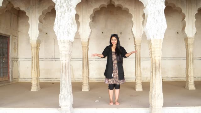 Mujer-India-saluda-namaste-da-la-bienvenida-a-invita-a-alegría-caliente-templo-antiguo-hindú-arquitectura-tradicional-pelo-negro-sonrisa-feliz-invitado-copia-estática-interior-casa-espacio-ancho-disparo-bloqueo-marco