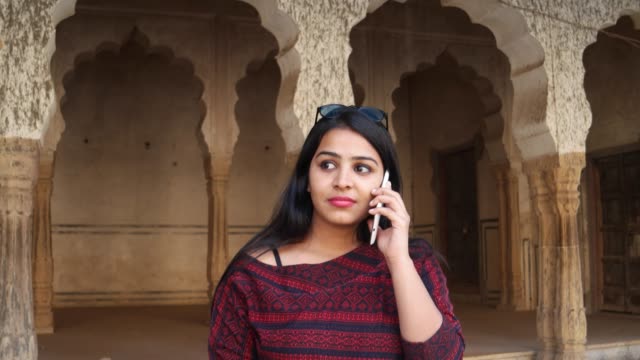 Handheld-Schuss-der-jungen-Frau-auf-ihrem-Handy-Handy-smart-kommunizieren,-Gespräche-Gespräche-Nachricht-Bildschirmtexte-berühren-Anteil-Netzwerk-Lächeln-vor-indischen-Architektur-Spalte-Bogen-Kulisse-hautnah