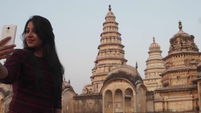 Woman-in-front-of-panoramic-attractive-ornate-temple-fort-palace-complex-from-a-vantage-point-higher-level-taking-selfie-photo-on-mobile-phone-camera-tourist--Hindu-religious-massive-love-handheld-pov