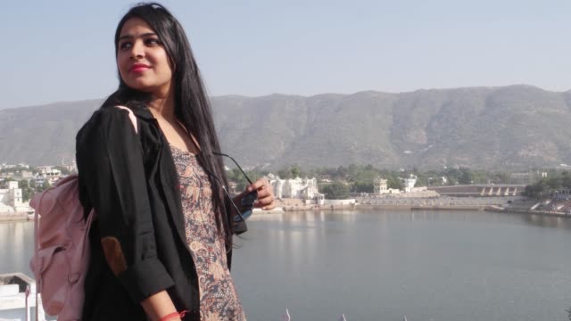 Handheld-woman-takes-selfie-photo-video-with-her-mobile-cellphone-device-from-a-panoramic-vantage-view-point-of-holy-Pushkar-lake,-a-sacred-city-for-Hindu-pilgrims-mela-festival-bathing-ghats-temples
