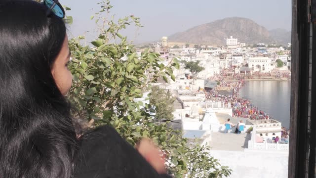 Handheld-Frau-nimmt-Selfie-Foto-Video-mit-ihrem-mobilen-Handy-Gerät-von-einem-Panorama-Aussichtspunkt-Blick-des-Heiligen-Pushkar-See,-eine-heilige-Stadt-für-Hindu-Pilger-Mela-Festival-Baden-Ghats-Tempel