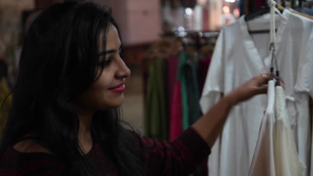 Schöne-junge-indische-Frau-einkaufen-Kleidung-Kleid-Stoff-am-Retail-Geschäft-Straßenhändler-am-Straßenrand-provisorischen-Shop-in-Rajasthan-glücklich-Content-selektiven-Fokus-bunte-handheld