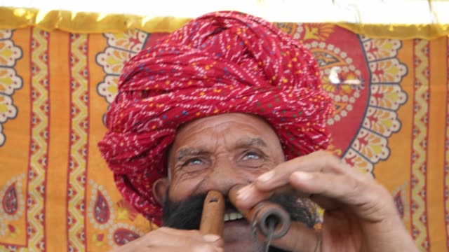 CU-Hand-held-Rajasthani-elderly-male-starts-to-play-the-flute-with-his-nose-in-front-of-a-colourful-fabric-tent