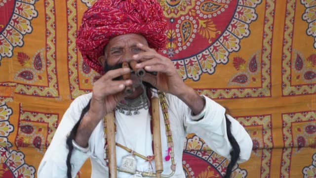 MS-Hand-held-Rajasthani-elderly-male-starts-to-play-the-flute-and-then-salutes-in-front-of-a-colourful-fabric-tent