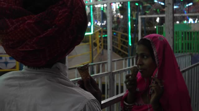 Indische-Paare-essen-Eis-in-traditionellen-Kleidern-im-Pushkar-Mela,-Karneval-von-Rajasthan,-Indien