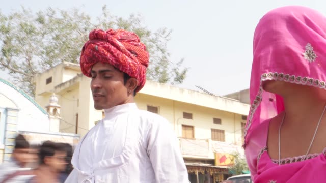 Hermosa-mujer-de-cardán-mano-en-sari-rosa-y-atractivo-hombre-de-turbante-rojo-caminando-en-Pushkar,-Rajasthan,-India