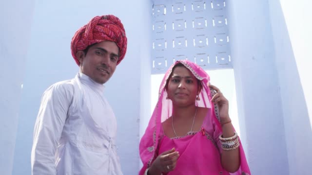 Frau-in-Rosa-Sari-und-Mann-mit-rotem-Turban-mit-hellblauem-Hintergrund-darstellen-für-Kamera-in-Rajasthan,-Indien