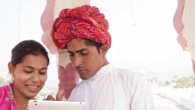 Pan-to-attractive-Indian-couple-working-learning-teaching-sharing-on-a-tablet-in-Rajasthan,-India