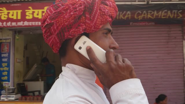 Rajasthani-junger-Mann-mit-rotem-Turban-gehen-und-sprechen-auf-dem-Handy-mobile-in-Pushkar,-Indien