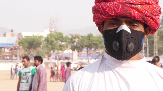 Indischer-Mann-mit-rotem-Turban-dreht-sich-und-ist-mit-einer-Verschmutzung-Maske-auf-einem-Rummelplatz-in-Indien
