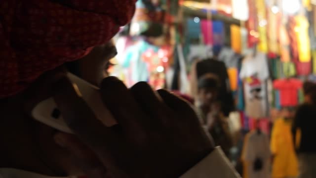 Hombre-indio-en-el-teléfono-móvil-hablando-y-caminando-con-turbante-de-Rajasthani-rojo-tradicional-en-la-noche