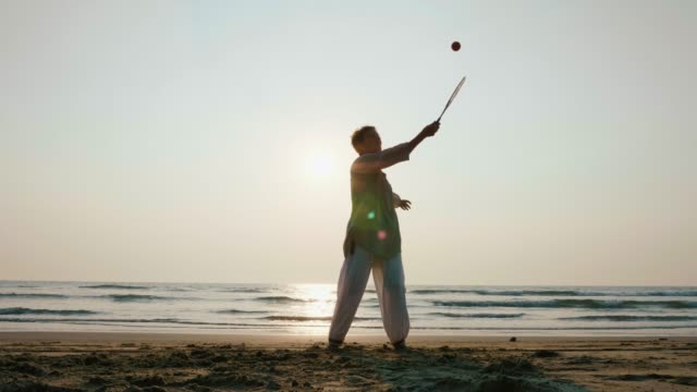 Ältere-Frau-praktizieren-Tai-Chi-Ballon-Ball-am-Strand-bei-Sonnenuntergang