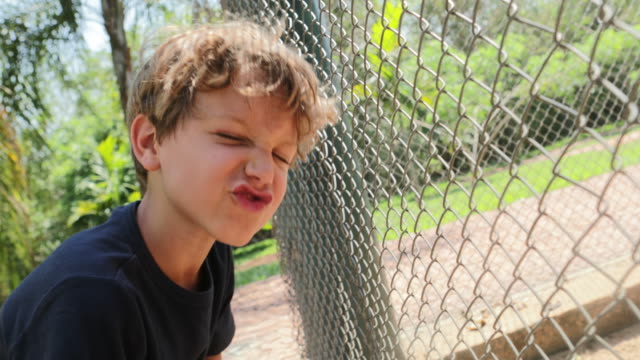 Little-boy-looking-at-animals-inside-cage-imitating-their-grounds-and-sounds.-Child-doing-funny-grimaces-expressive-faces-as-if-he-was-a-monkey