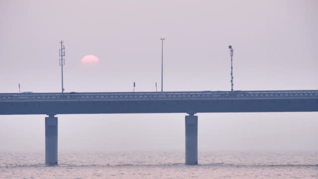 Fahrzeuge,-die-auf-einer-modernen-Brücke-vorbei,-während-im-Hintergrund-Sonne-untergeht