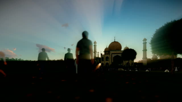 Taj-Mahal-with-tourists-walking-against-beautiful-sunset,-panning-4K
