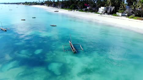 Aerial-view-of-a-fisherman-sails-on-a-wooden-boat-on-clear-blue-water-along-a-tropical-exotic-beach-in-Africa