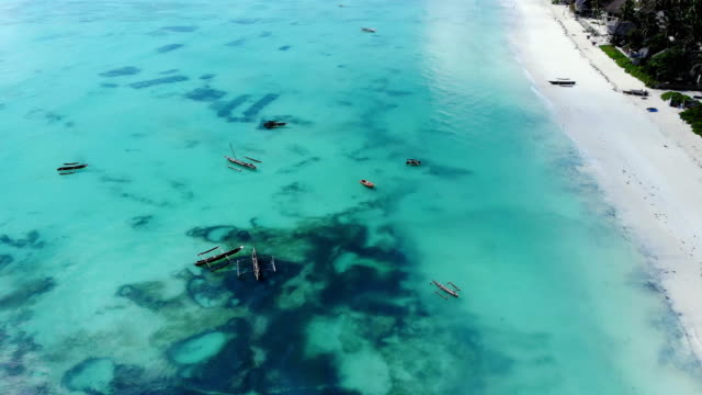 Vista-aérea-de-un-pescador-navega-en-un-barco-de-madera-en-agua-azul-clara-a-lo-largo-de-una-playa-exótica-tropical-en-África