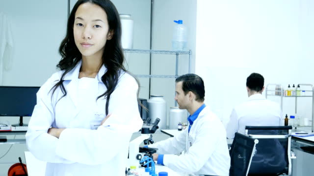 Asiatische-Wissenschaftlerinnen-oder-Chemiker-auf-Kamera-mit-attraktiven-Lächeln.-Team-Wissenschaftler-in-einem-Labor-zusammenarbeiten.-4K-Auflösung.