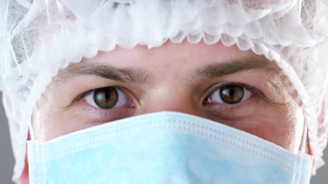 Ein-Porträt-von-einem-Arzt-oder-Chirurgen-in-einer-medizinischen-Maske,-eine-Atemschutzmaske,-braune-Augen,-ein-OP-Cap,-in-einem-Krankenhaus-oder-einer-Klinik.