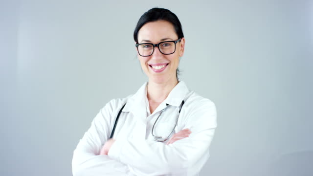 Porträt-von-einer-Ärztin-mit-weißen-Kittel-und-Stethoskop-lächelnd-Blick-in-Kamera-auf-weißem-Hintergrund.
