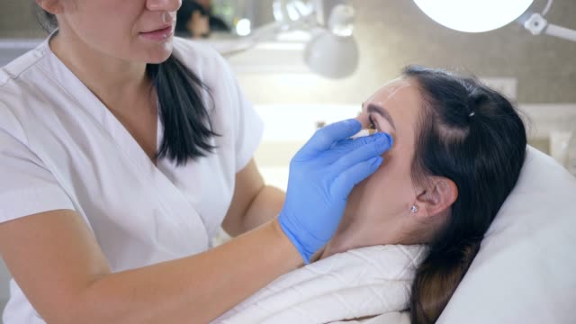 Arzt-in-Handschuhen-markiert-Problemzonen-im-Gesicht-des-Mädchens-mit-weißen-Stift-im-Beauty-Salon,-Verjüngung-Verfahren