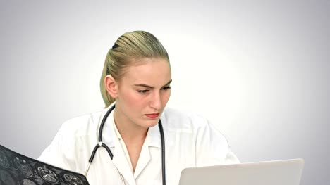 Young-female-doctor-examining-xray-writing-down-results-diagnosis-to-laptop-computer-on-white-background
