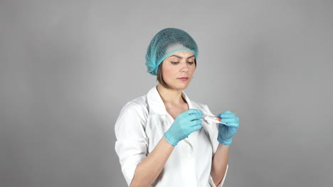Junge-Ärztin-in-Handschuhe-halten-eine-Spritze-auf-grauem-Hintergrund-isoliert.-Medizinisches-Konzept.-Schuss-in-4k