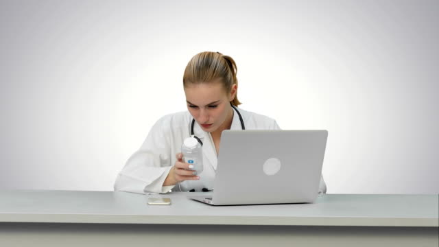 Retrato-de-una-enfermera-estudio-nuevo-las-píldoras-utilizando-equipo-portátil-sobre-fondo-blanco