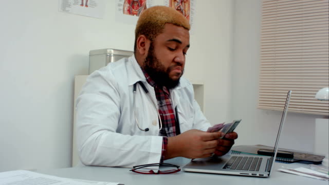Young-male-doctor-counting-money-at-his-desk