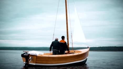 Holz-Segelboot-mit-zwei-Männern,-die-versuchen,-Mast-gesetzt