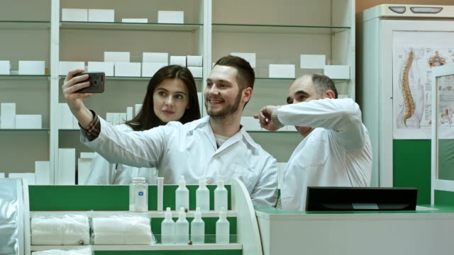 Cheerful-team-of-pharmacist-and-interns-take-selfie-via-smartphone-at-workplace