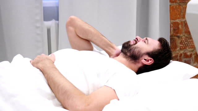 Bart-Mann-mit-Nackenschmerzen,-die-versuchen-sich-zu-entspannen-im-Bett