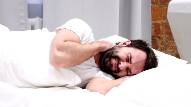 Hombre-de-barba-con-dolor-en-el-cuello-tratando-de-relajarse-en-la-cama