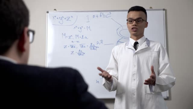 A-young-successful-African-scientist-in-a-white-coat-and-glasses,-stands-at-the-blackboard-with-formulas,-presentation,-lecture,-training-concept.-60-fps