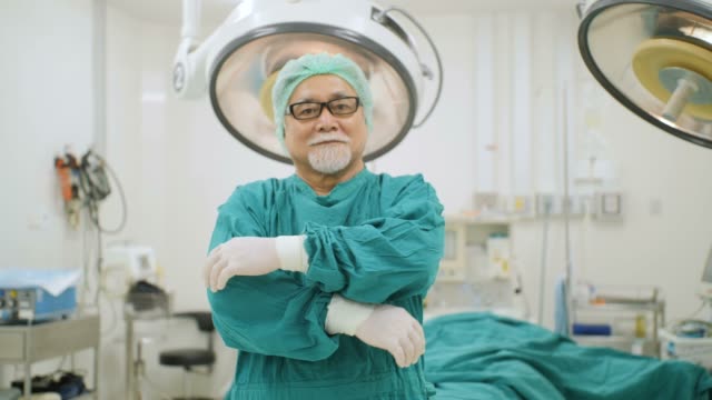 Porträt-von-senior-männlichen-Chirurg-tragen-volle-chirurgische-scheuert-sich-lächelnd-Kamera-im-Operationssaal-im-Krankenhaus.