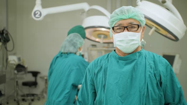 Retrato-de-senior-masculino-cirujano-usar-completo-quirúrgico-friega-cámara-sonriente-con-los-médicos-del-equipo-operando-en-paciente-en-quirófano-en-el-hospital.