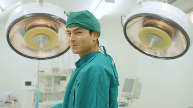 Porträt-des-kaukasischen-männliche-Chirurgen-tragen-volle-chirurgische-scheuert-sich-lächelnd-Kamera-im-Operationssaal-im-Krankenhaus.