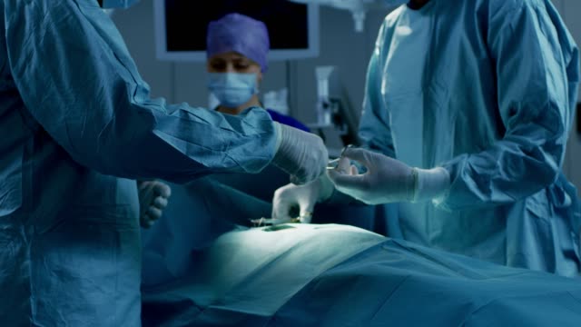 In-the-Hospital-Operating-Room-Diverse-Team-of-Professional-Surgeons-and-Nurses-Suture-Wound-after-Successful-Surgery.
